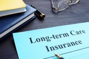 A photo of a blue paper with the words "Long-term Care Insurance" with a pair of glasses, some books and a pen