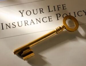 A photo of a shaded paper that reads "Your Life Insurance Policy" with a large gold key laying on it