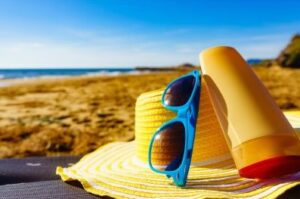 Picture of a straw hat, sunscreen and a pair of sunglasses symbolizing summer and being in the sun.