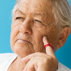 A photo of an older person wit a red thread around their finger while thinking, symbolizing age-related memory loss